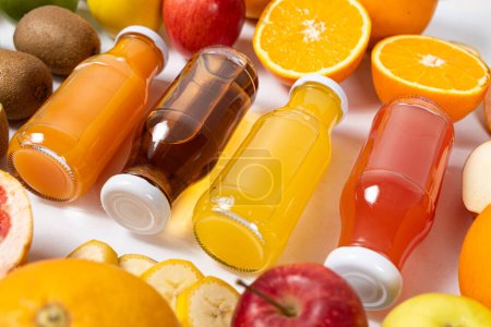 Photo for Assortment of fruit juices in glass bottles among fruits on white background top view. - Royalty Free Image