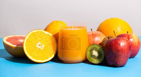 Photo for Multifruit juice in a glass among fresh fruits on blue and white background. - Royalty Free Image