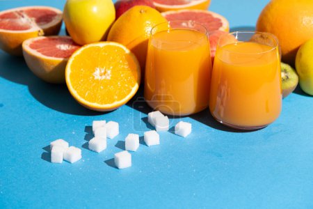Sugar content in fruit juices. Sugar cubes and glasses of multifruit juice