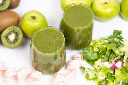 A green smoothie in a glass and a measuring tape. A healthy drink for weight loss.