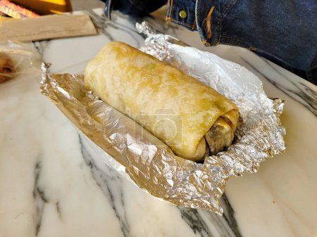 Un burrito délicieux fraîchement fait et enveloppé dans du papier d'aluminium s'assoit sur une table en marbre élégant, prêt à être apprécié