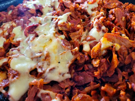Gros plan sur l'appétissante viande Al Pastor recouverte de fromage fondu, servie chaude dans une poêle