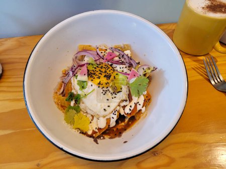 A deep plate full of chilaquiles topped with a perfectly fried egg with coffee, breakfast