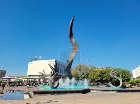 Foto de Guadalajara, México - 20 de marzo de 2023: Una impresionante escultura moderna y fuente ocupa el centro del escenario en una bulliciosa plaza de Guadalajara - Imagen libre de derechos