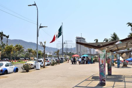 Photo for Acapulco, Mexico - April 27 2024:A busy street with a flag flying in the background. There are many people walking around and cars parked along the street - Royalty Free Image