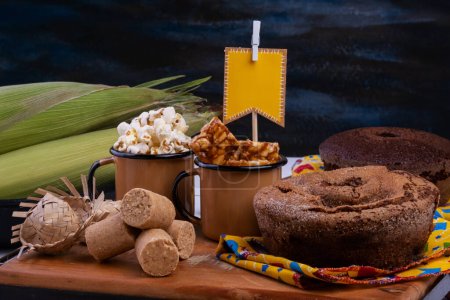 Papierfahne, Kuchen, Popcorn und Süßigkeiten von der Festa Junina auf schwarzem Holztisch.