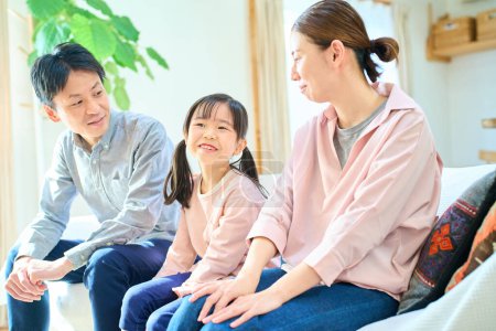 Téléchargez les photos : Parents et leur enfant parlent heureux dans le salon - en image libre de droit