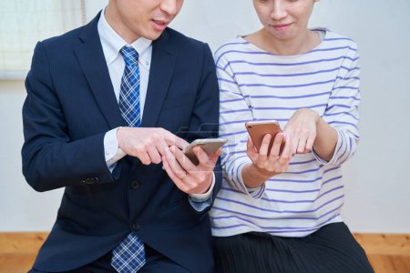 Téléchargez les photos : Un couple consultant tout en regardant un écran de smartphone dans la chambre - en image libre de droit