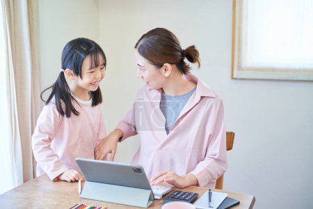 Téléchargez les photos : Une fille se blottissant contre sa mère qui se dirige vers l'ordinateur à la maison - en image libre de droit