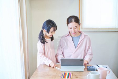Photo for A girl snuggling up to her mother who is heading to the computer at home - Royalty Free Image