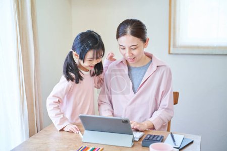 Téléchargez les photos : Une fille se blottissant contre sa mère qui se dirige vers l'ordinateur à la maison - en image libre de droit