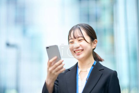 Photo for Young woman in suit looking at the screen of smartphone - Royalty Free Image