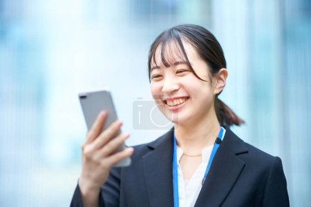 Téléchargez les photos : Jeune femme en costume regardant l'écran du smartphone - en image libre de droit
