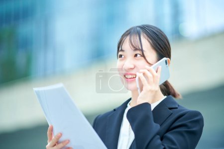 Photo for Asian young woman in a suit talking on a smartphone - Royalty Free Image