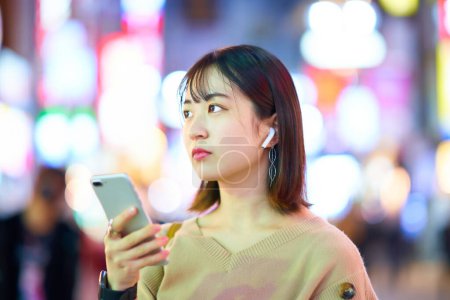 Foto de Mujer joven mirando el teléfono inteligente en el centro por la noche - Imagen libre de derechos