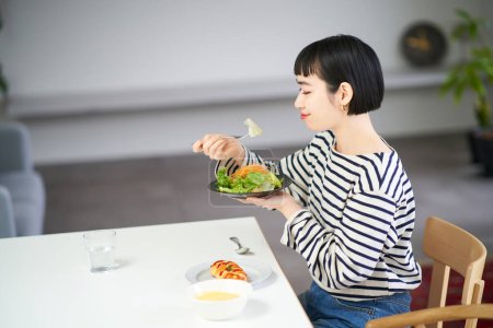Téléchargez les photos : Jeune femme manger à la maison - en image libre de droit