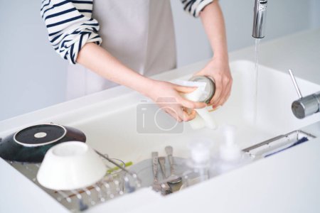 Téléchargez les photos : Jeune femme lavant la vaisselle dans la cuisine - en image libre de droit