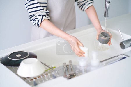 Téléchargez les photos : Jeune femme lavant la vaisselle dans la cuisine - en image libre de droit