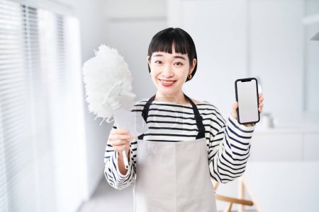 Foto de Mujer joven con herramientas de limpieza y teléfono inteligente en la habitación - Imagen libre de derechos