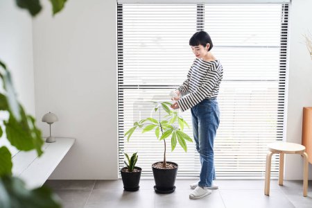 Téléchargez les photos : Jeune femme prenant soin des plantes d'intérieur dans la chambre - en image libre de droit