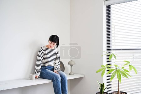 Téléchargez les photos : Une jeune femme se relaxant dans une chambre aux plantes d'intérieur - en image libre de droit