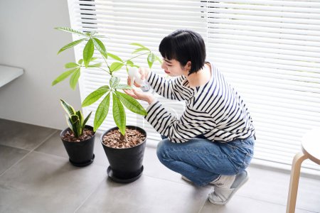 Young woman taking care of houseplants in the room
