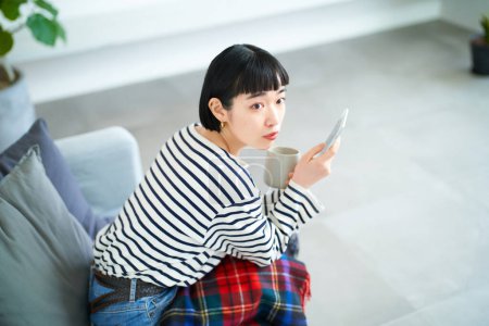 Téléchargez les photos : Jeune femme opérant un smartphone dans la chambre - en image libre de droit