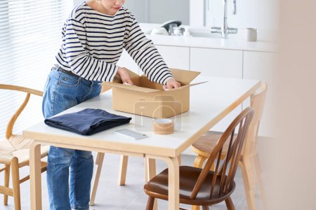 Photo for Young woman packing clothes into cardboard in the room - Royalty Free Image