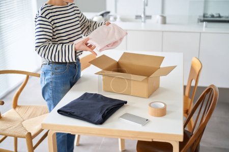 Photo for Young woman packing clothes into cardboard in the room - Royalty Free Image