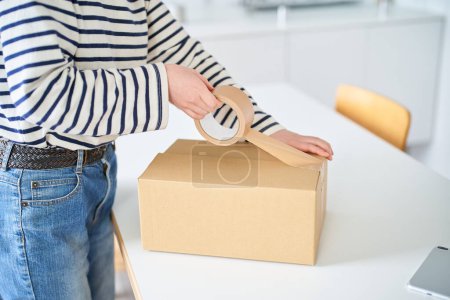 Téléchargez les photos : Jeune femme emballant une boîte en carton dans la chambre - en image libre de droit