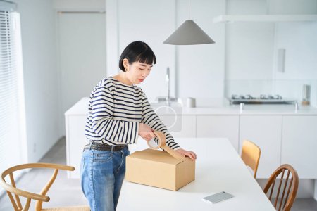Photo for Young woman packing a cardboard box in the room - Royalty Free Image