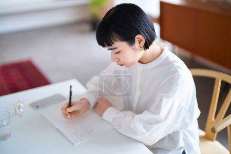 Téléchargez les photos : Jeune femme écrit dans un cahier dans la chambre - en image libre de droit