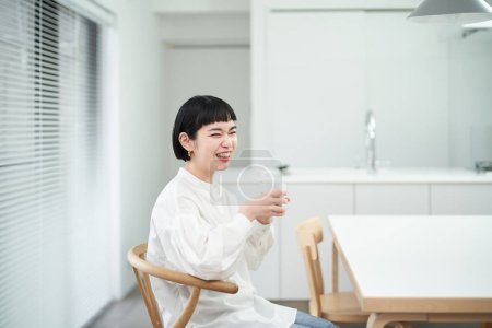 Téléchargez les photos : Jeune femme boire de l'eau dans une chambre calme - en image libre de droit