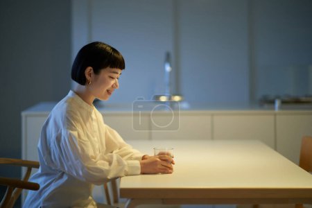 Téléchargez les photos : Jeune femme boire de l'eau dans une chambre calme - en image libre de droit