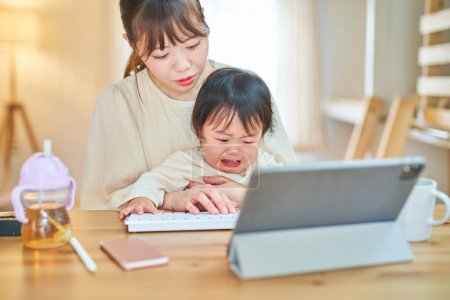 Téléchargez les photos : Une femme qui utilise une tablette PC et un bébé en pleurs à la maison - en image libre de droit