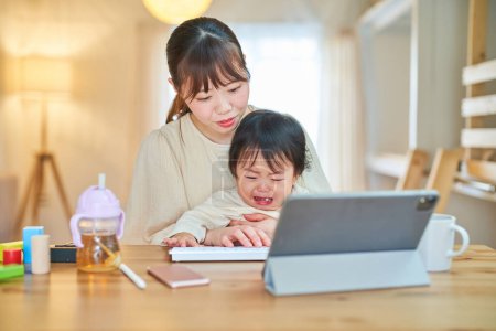 Téléchargez les photos : Une femme qui utilise une tablette PC et un bébé en pleurs à la maison - en image libre de droit