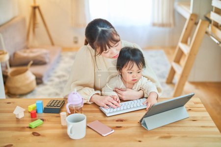 Photo for Young mother holding a baby and operating a computer - Royalty Free Image