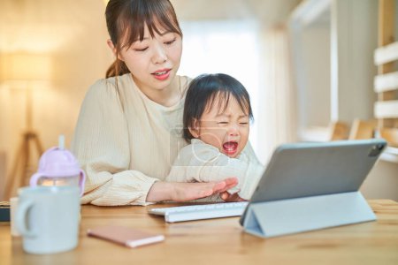 Téléchargez les photos : Une femme et un nourrisson qui actionnent une tablette PC avec une expression fatiguée à la maison - en image libre de droit