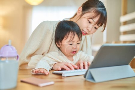 Téléchargez les photos : Une femme et un nourrisson qui actionnent une tablette PC avec une expression fatiguée à la maison - en image libre de droit