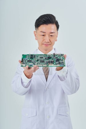 Foto de Un hombre con una bata blanca con un circuito electrónico y fondo blanco - Imagen libre de derechos