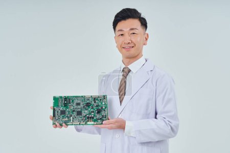 Foto de Un hombre con una bata blanca con un circuito electrónico y fondo blanco - Imagen libre de derechos