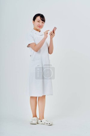 Téléchargez les photos : Une femme vêtue d'un manteau blanc utilisant un smartphone et un fond blanc - en image libre de droit