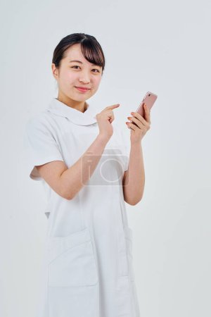 Téléchargez les photos : Une femme vêtue d'un manteau blanc utilisant un smartphone et un fond blanc - en image libre de droit