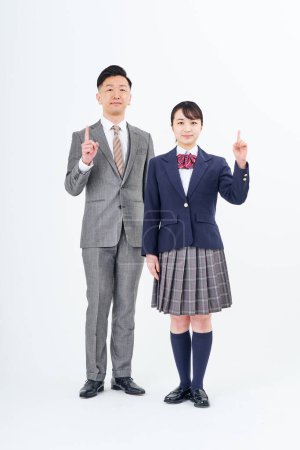 Téléchargez les photos : A man and a high school girl in a suit posing with their index finger up and white background - en image libre de droit