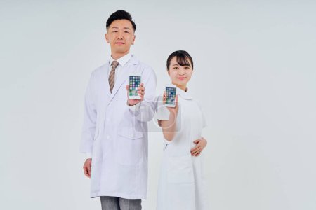 Foto de Hombre y mujer con batas blancas operando teléfonos inteligentes y fondo blanco - Imagen libre de derechos