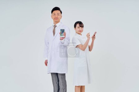 Foto de Hombre y mujer con batas blancas operando teléfonos inteligentes y fondo blanco - Imagen libre de derechos
