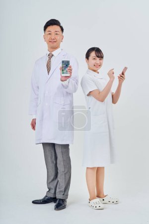 Foto de Man and woman wearing white coats operating smartphones and white background - Imagen libre de derechos