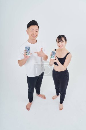Téléchargez les photos : Homme et femme en vêtements de sport avec smartphones et fond blanc - en image libre de droit