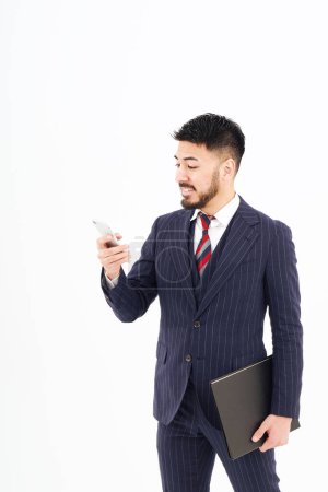 Photo for A man in a suit operating a smartphone and white background - Royalty Free Image