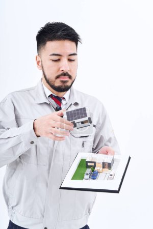 Photo for A man in work clothes with a house model and white background - Royalty Free Image